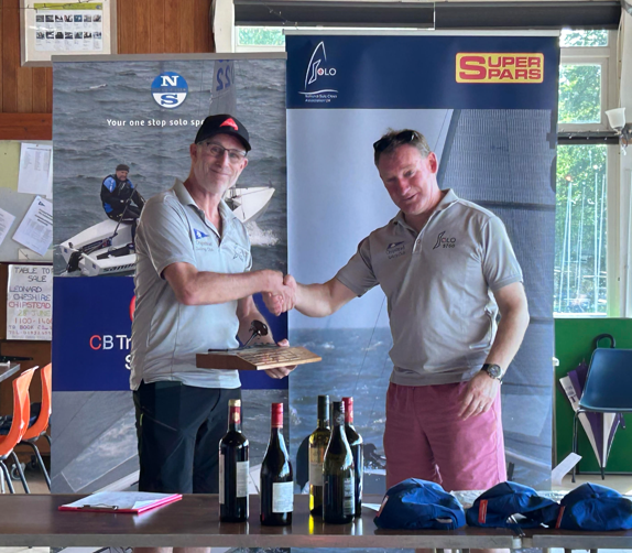 two-men-shaking-hands-in-front-of-a-table-with-bot Two men shaking hands in front of a table with bottles of wine AI-generated content may be incorrect.